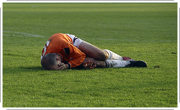 soccer player holding head, curled up in pain on ground