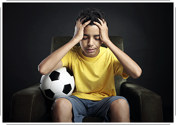 student athlete holding head with soccer ball beside him 