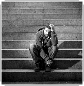 black/white photo of young forlorn man sitting on cements stair steps
