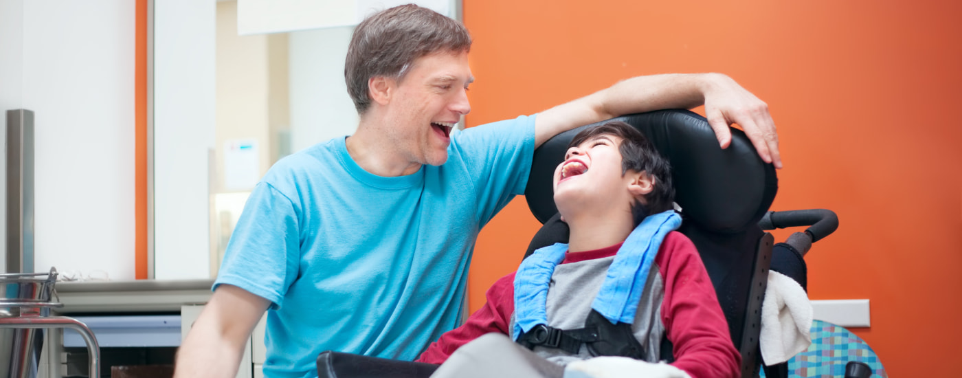 Father and his son in a wheel chair laughing and smiling at each other.
